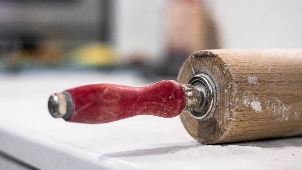 Detailed image of a vintage rolling pin with a red handle against a white background.